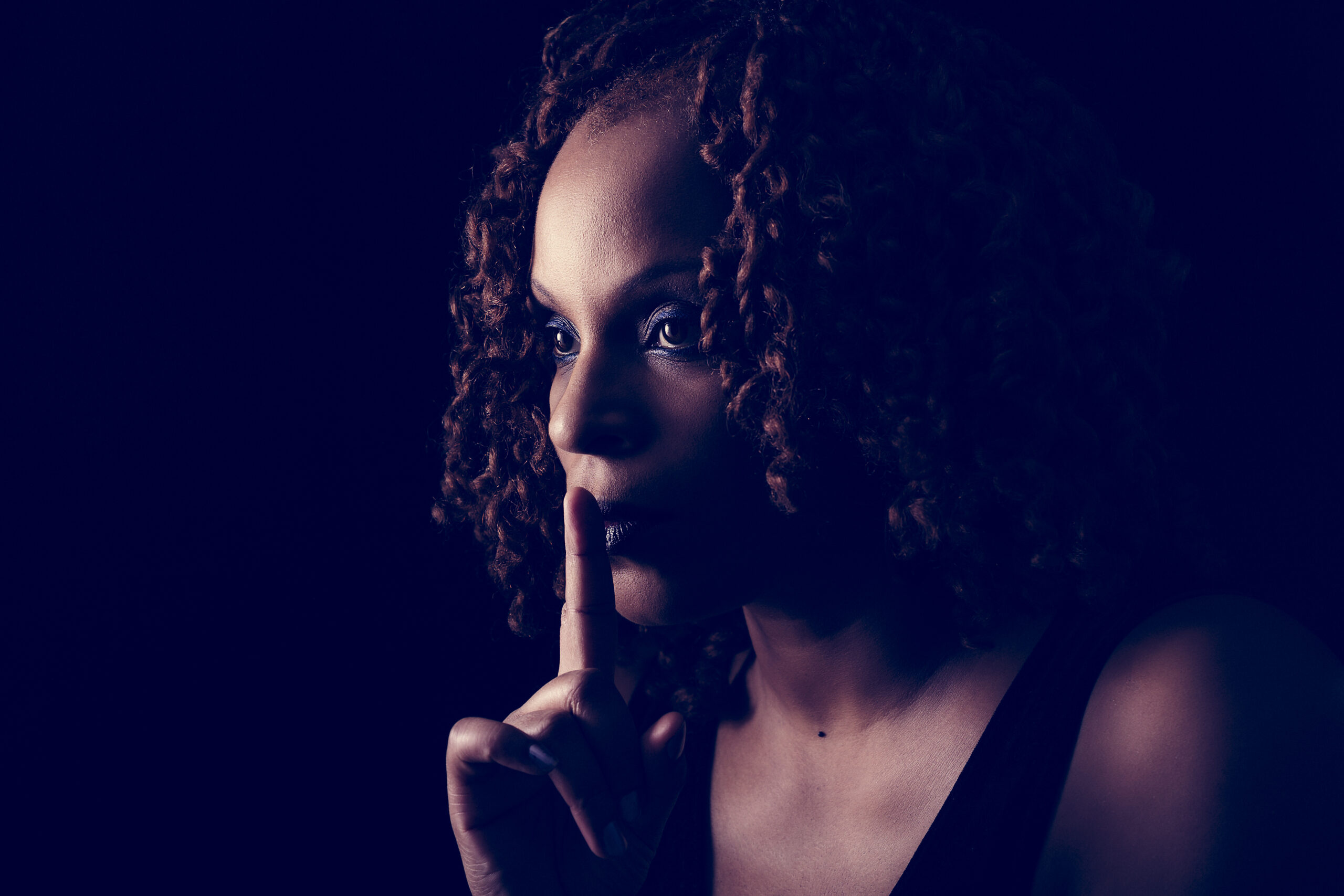 Black woman with finger over her mouth in a motion that means be quiet 